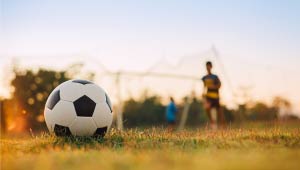 A picture of a soccer ball with a soccer player in the background on a soccer field.