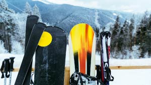 A picture of skis and snowboards leaning against a rail, overlooking a snowy ski slope.