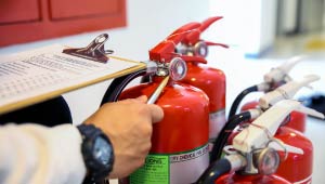 Person with checklist inspecting fire extinguishers.